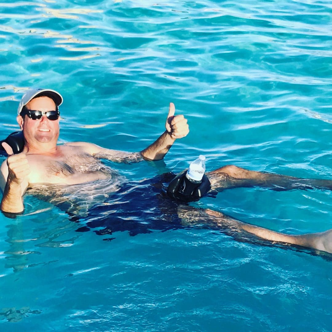 Man floating in turquoise water, thumbs up